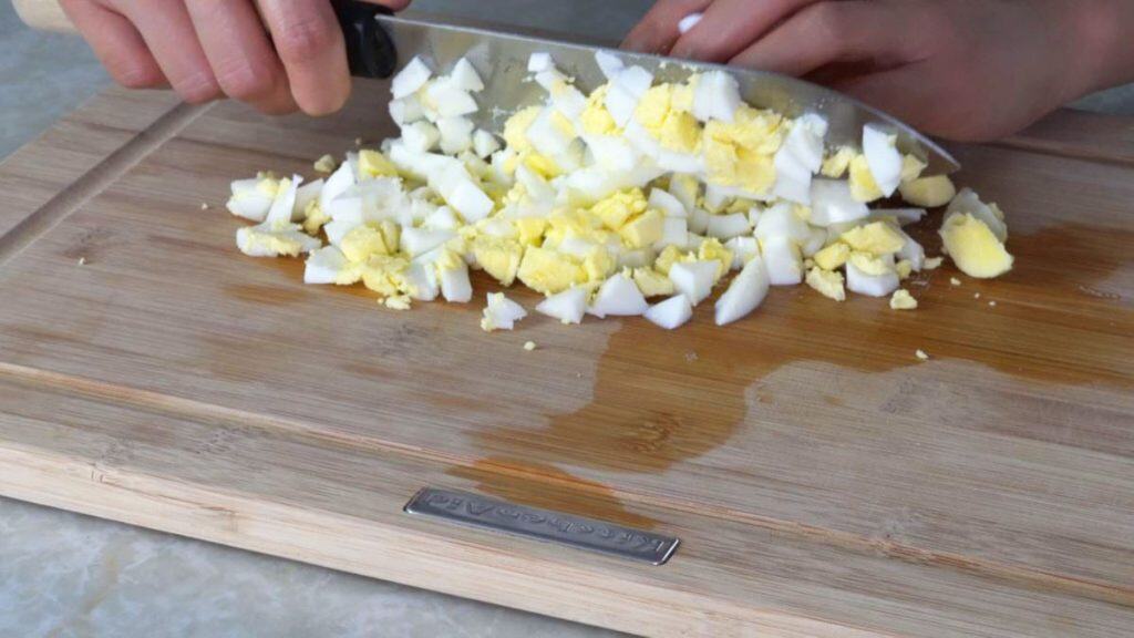 Mincing hardboiled eggs with a knife on a wooden cutting board