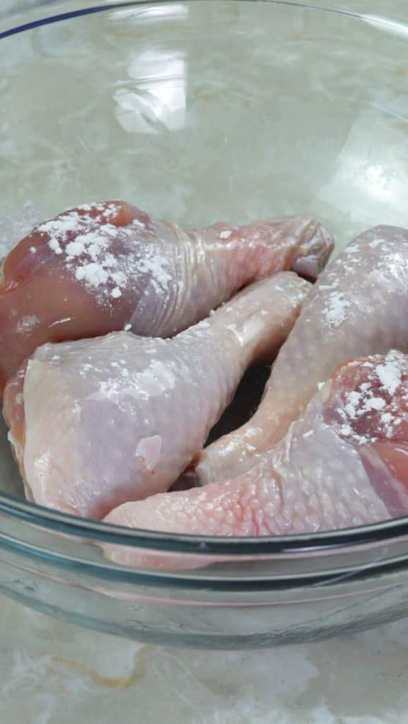 Raw chicken thighs coated with oil and baking powder in a glass bowl