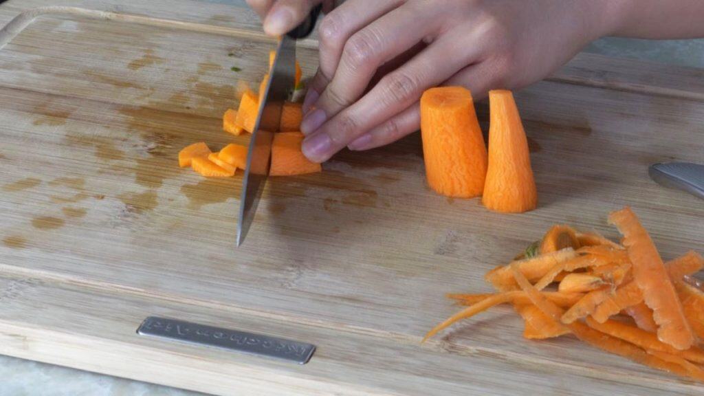 Slicing carrots with a knife on a wooden cutting board