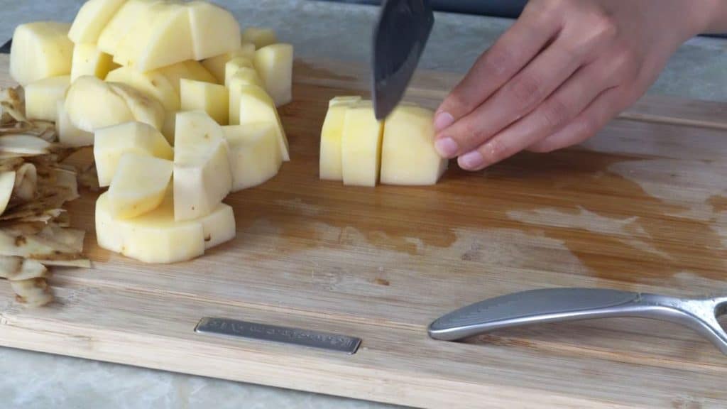 Dicing potatoes with a knife on a wooden cutting board