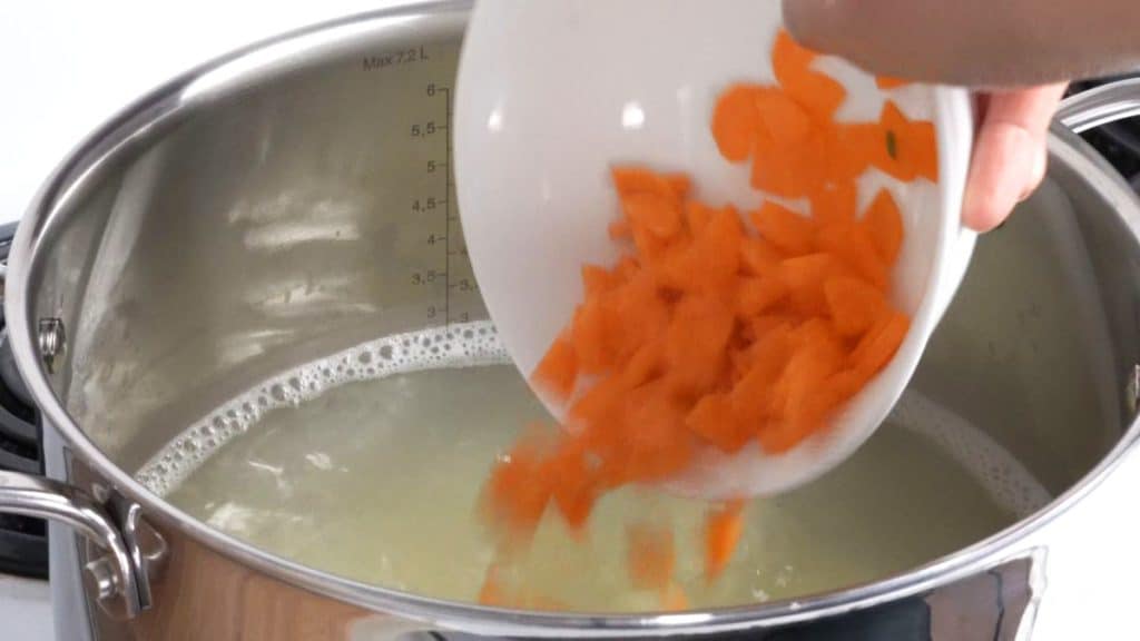 Adding sliced carrots to a pot of boiling water with potatoes