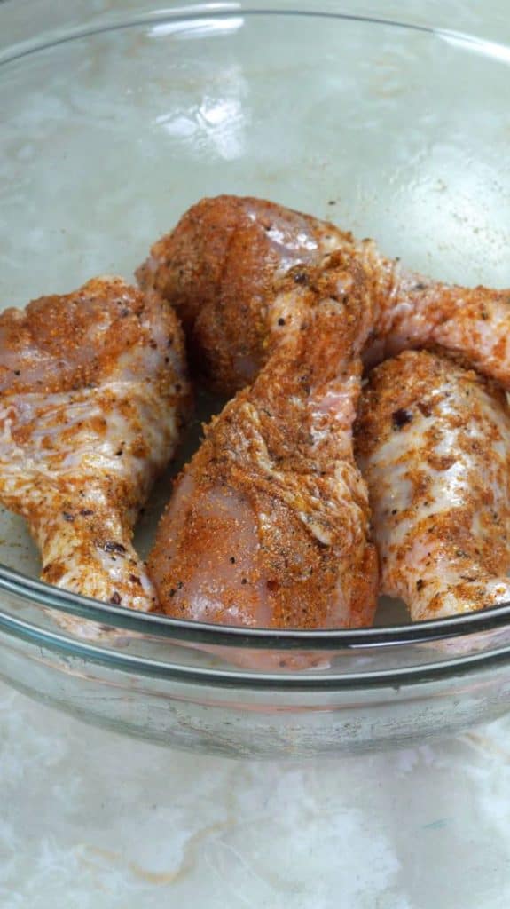Raw chicken drumsticks coated with spices in a glass bowl