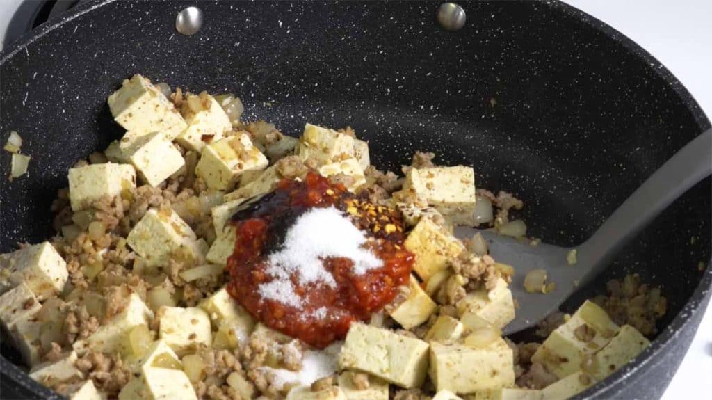Chili garlic sauce, oyster sauce, sugar and red pepper flakes on top of diced medium firm tofu and ground pork in a pan