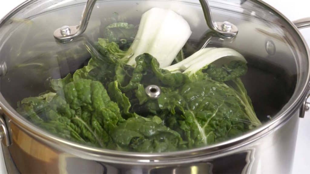 Steaming and boiling baby bok choy in a large pot covered