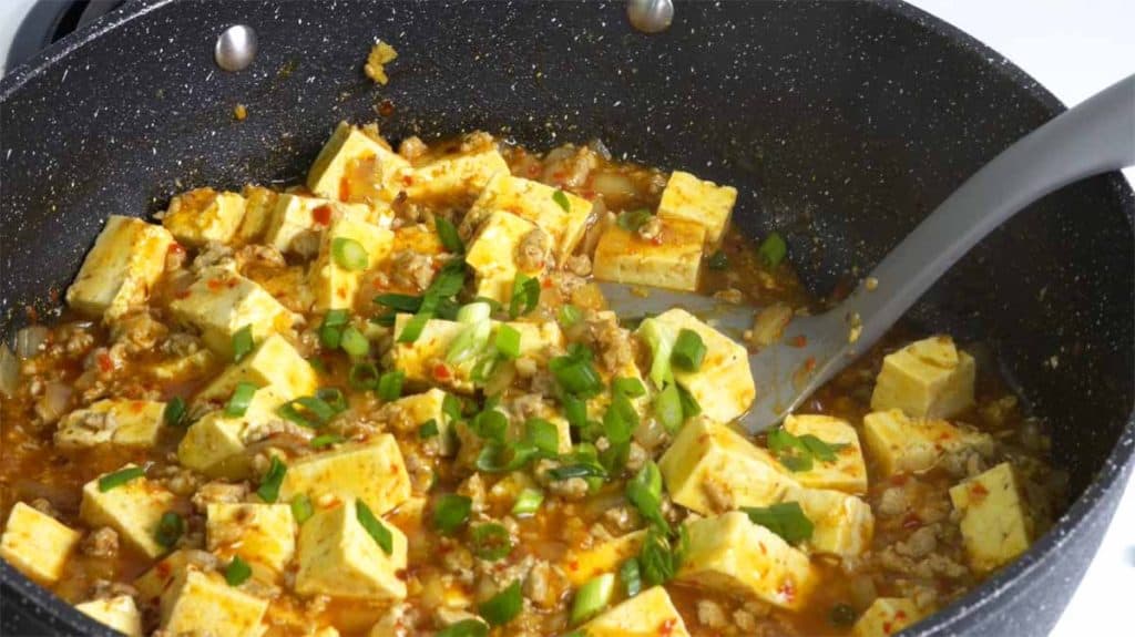 Mapo tofu topped with chopped green onion in a pan