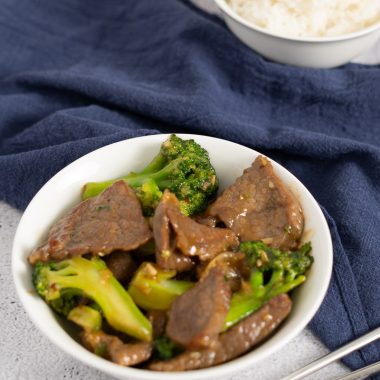 Beef and broccoli in a white bowl with a bowl of steamed white rice