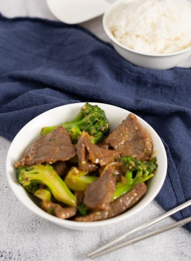 Beef and broccoli in a white bowl with a bowl of steamed white rice