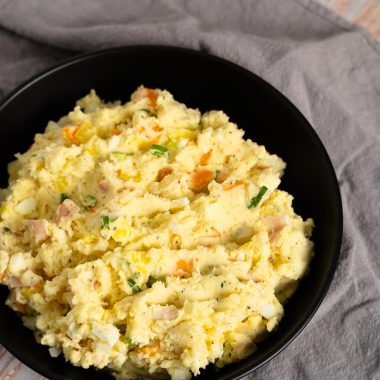 Japanese potato salad with egg, green onions, carrot, potatoes and ham in a black bowl on a gray towel on a wooden surface