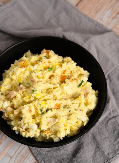 Japanese potato salad with egg, green onions, carrot, potatoes and ham in a black bowl on a gray towel on a wooden surface