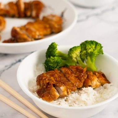 Sliced teriyaki chicken with broccoli on steamed white rice in a white bowl on a marble surface