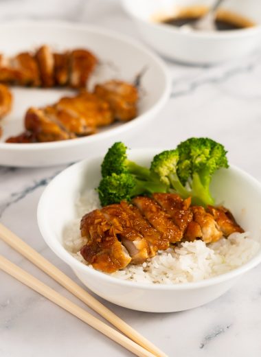 Sliced teriyaki chicken with broccoli on steamed white rice in a white bowl on a marble surface